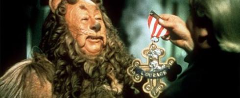 The photograph is an image of a character known as The Cowardly Lion from the movie "Wizard of Oz." In this photograph, the Lion is being presented a medal that includes red gems and the word "Courage" in a gold setting, as the Wizard recognizes the Lion for having courage of the heart to act in new ways in the world.